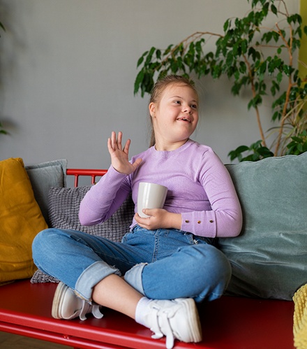 Young girl in a violet sweater sitting on a couch and waving